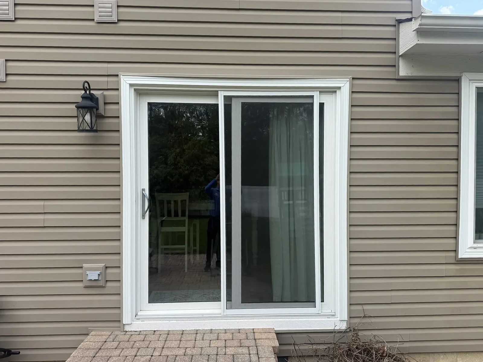 New sliding patio door with white trim against tan siding