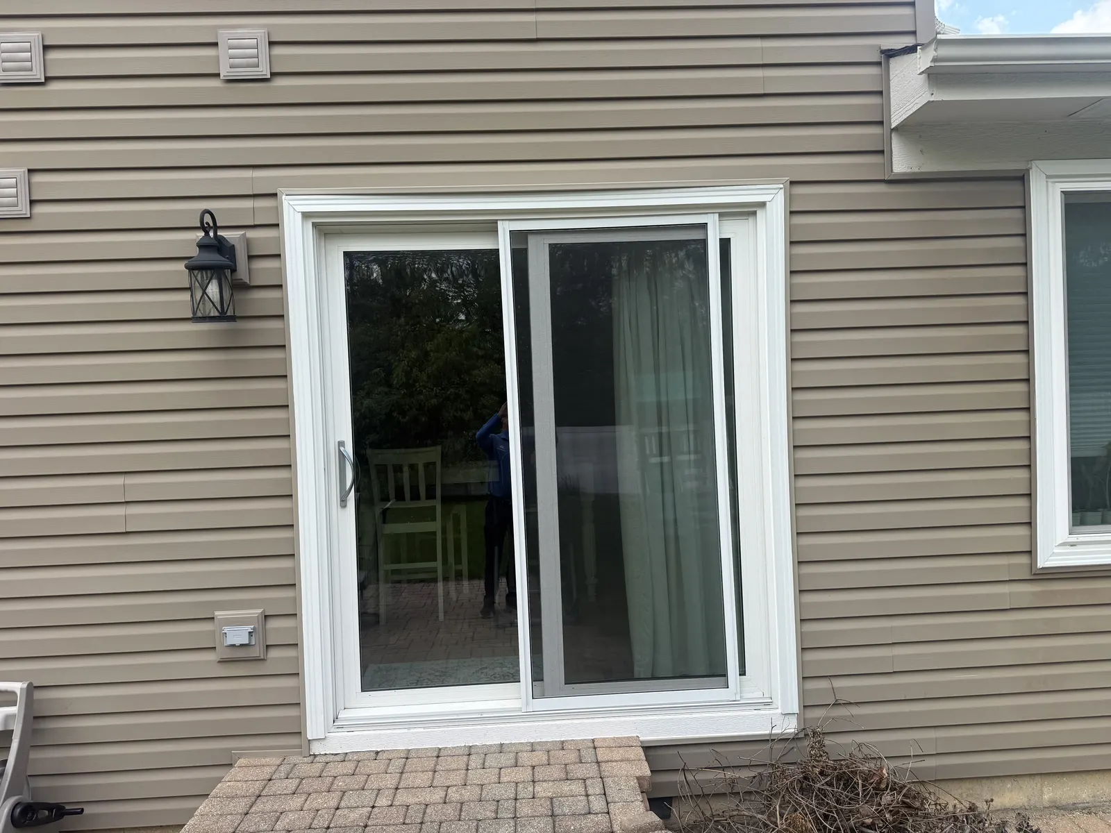 New sliding patio door with white trim against tan siding